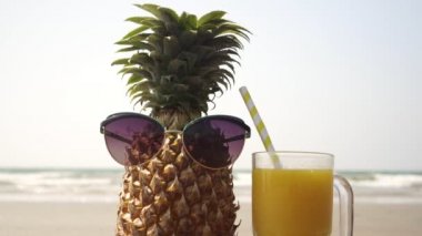 Güneş gözlüklü komik ananas ve denizin arka planında bir bardak meyve suyu.