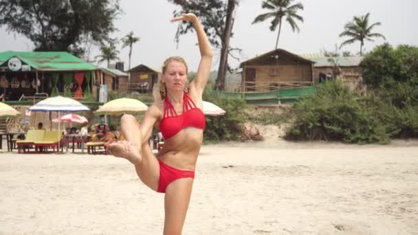 Молода приваблива жінка в купальнику займається гіастикою і спортом на пляжі — стокове відео