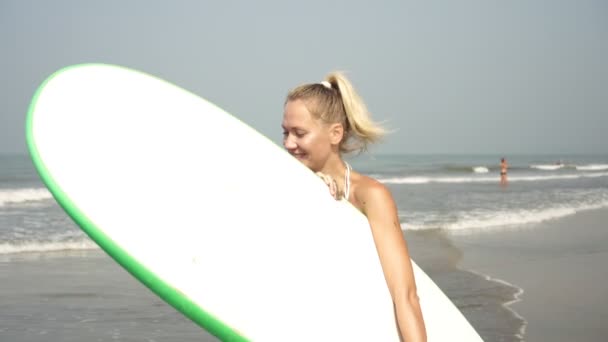 Ung aktiv kvinna surfar promenader längs havet stranden med en surfing — Stockvideo