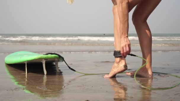 Egy női szörfös pórázt köt a lábához, és szörfözni megy a tengerbe.. — Stock videók