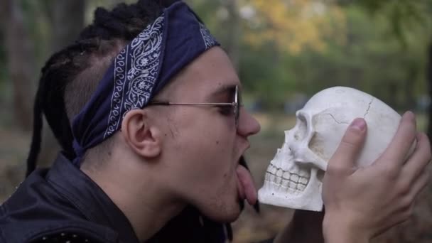 En punkare slickar en mänsklig skalle med tungan. Begreppet för Halloween — Stockvideo
