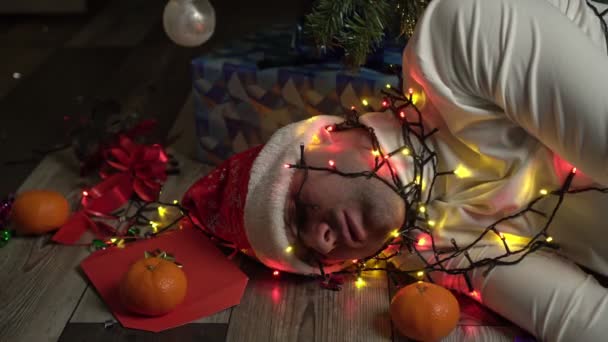 Zabawny człowiek ze świecącą girlandą na głowie śpi po przyjęciu świątecznym lub noworocznym. — Wideo stockowe
