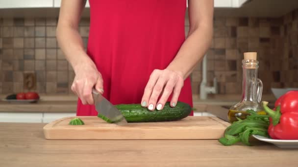 Woman preparing salad in the kitchen. Woman cuts a cucumber with a knife in the kitchen — Stock Video