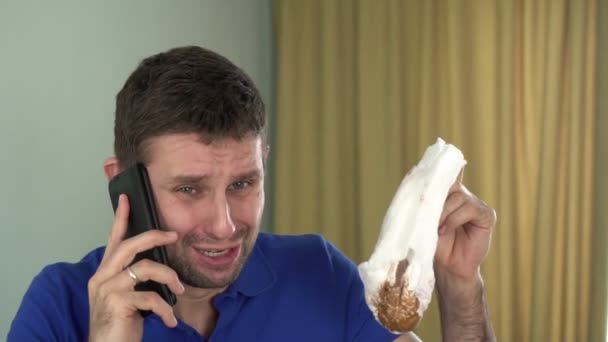 Молодой напуганный несчастный мужчина с грязным детским подгузником разговаривает по телефону — стоковое видео