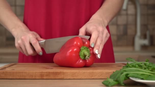 Una mujer en la cocina corta un pimentón rojo con un cuchillo en la cocina — Vídeos de Stock