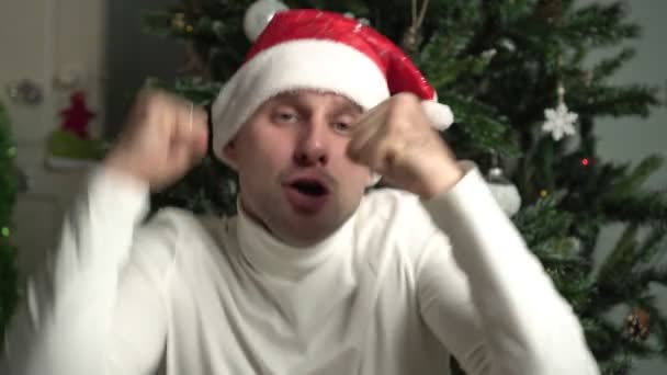 Nový rok nebo Vánoce, portrét mladého veselého šťastného muže. Emocionální muž tančí v Santově klobouku — Stock video