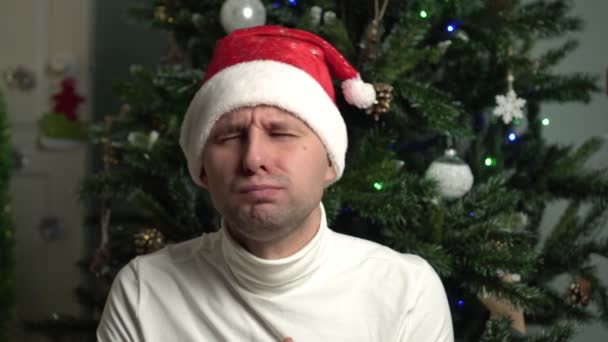 Kerstmis, een man met een kerstmuts eet een mandarijn fruit op de achtergrond van het nieuwe jaar boom — Stockvideo