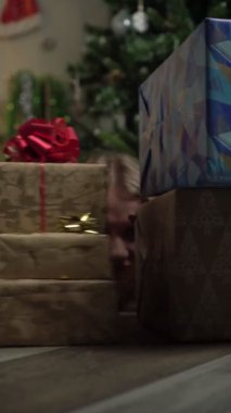 Yılbaşı ve Noel. Genç bir kadın hediye kutularının arkasına saklanır. Dikey video