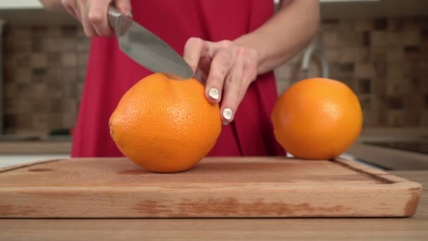 Mulher na cozinha corta laranjas suculentas com uma faca, câmera lenta — Vídeo de Stock
