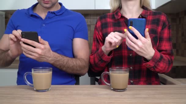 Молодая пара, семья, мужчина и женщина со смартфонами дома на кухне. Концепция интернет-зависимости — стоковое видео