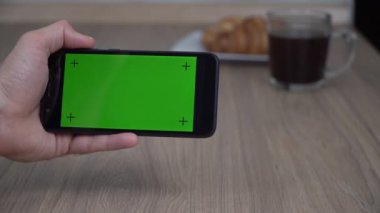 Smartphone with a green screen. A man in the kitchen is holding a phone with a blank green display