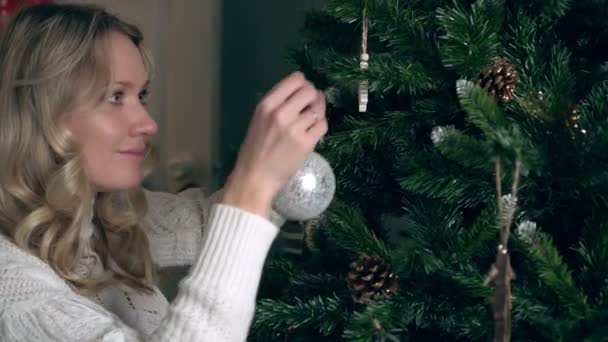 Молодая женщина украшает елку дома новогодними игрушками — стоковое видео