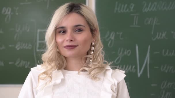 Portret van een jonge aantrekkelijke lerares in een schoolklas. jonge schooljuf, close-up — Stockvideo