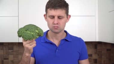 Mutfakta çiğ brokoli yiyen aç, üzgün bir adam. Yemek pişiremeyen bir adamın portresi. Mutsuz vejetaryen