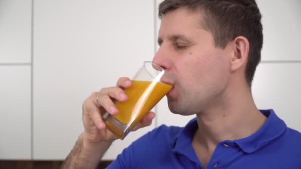 Un jeune homme dans la cuisine boit du jus de fruit dans un verre — Video