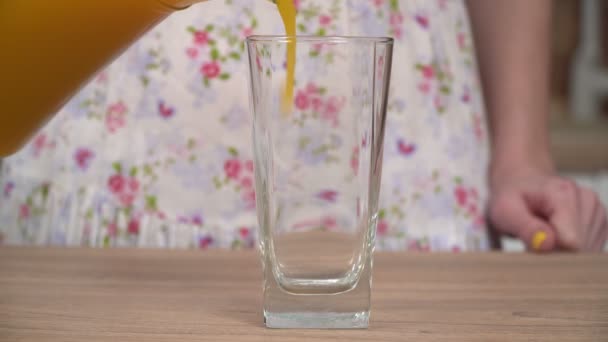Μια γυναίκα στην κουζίνα χύνει φρέσκο χυμό από μια κανάτα σε ένα ποτήρι. Ένα ποτήρι φρέσκο χυμό, κοντινό πλάνο — Αρχείο Βίντεο