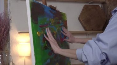 Yenilikçi bir sanatçı, elleri ve parmaklarıyla tuvale resim çizer. Bir kadın sanatçı ellerini kullanarak parlak renklerle bir resim çizer. Çağdaş sanat