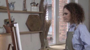 Ciddi kadın ressam bir stüdyoda konsantrasyonlu bir resim çizer.