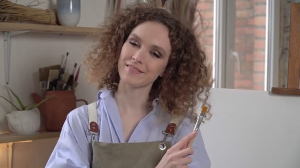 Mooie jonge vrouw kunstenaar op de achtergrond van een wit doek of schilderij — Stockvideo