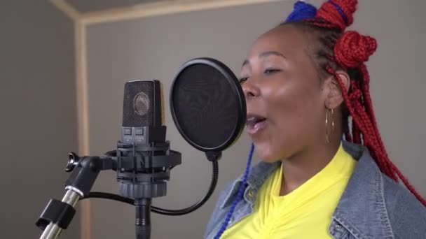 Giovane cantante afroamericano attraente sorride e canta in un microfono durante la registrazione in uno studio di musica. — Video Stock