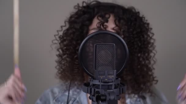Young attractive woman singer singing into a microphone in a professional recording studio. — Stock Video