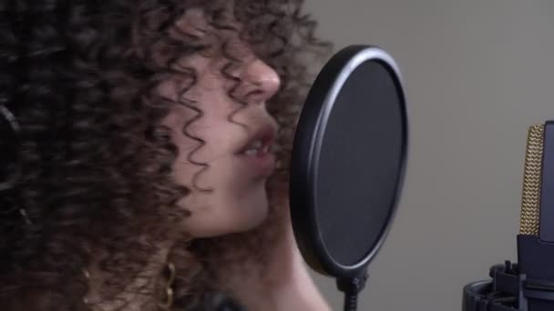 Portrait of a young black singer. Woman with headphones sings into a microphone in a recording studio. — Stock Video