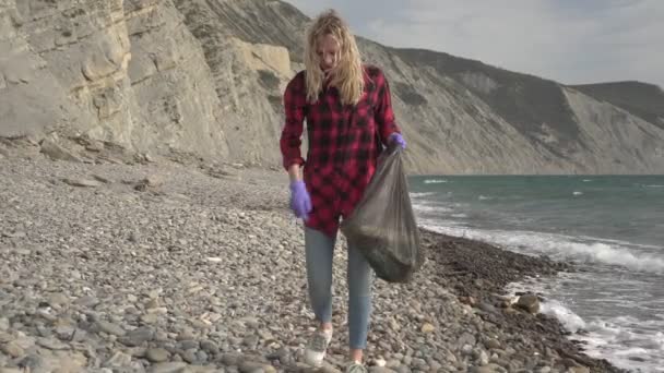 Voluntário ecologista pessoa remove lixo na praia. Uma mulher limpa a costa do mar do lixo — Vídeo de Stock