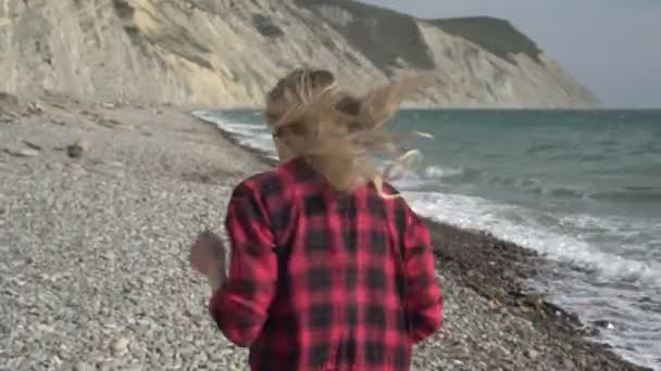 Joven mujer feliz corre a la playa del mar. Una hermosa mujer camina a lo largo de la costa salvaje del mar — Vídeos de Stock