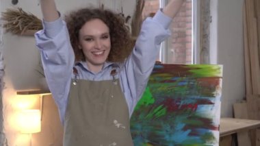 Soyut bir tablonun arka planında neşeli, mutlu, modern bir kadın sanatçı var.