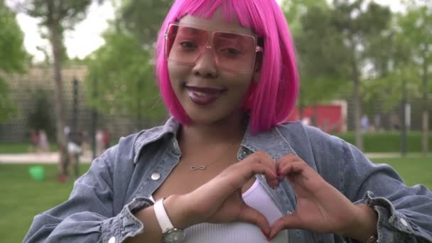 Jeune femme noire brillante aux cheveux roses montre un signe de coeur avec sa main — Video