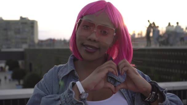 Jovem mulher negra atraente com cabelo rosa mostra sinal do coração com os dedos — Vídeo de Stock