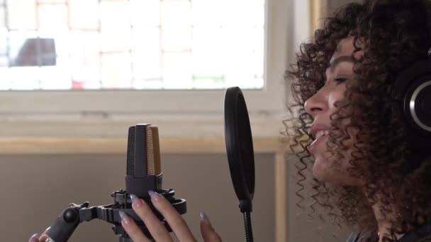 Молодая привлекательная певица в наушниках поет в микрофон в студии звукозаписи. Медленное движение — стоковое видео