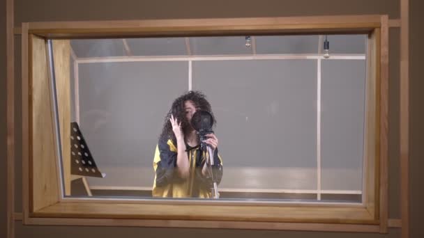 Un cantante contemporaneo alla moda sta registrando una nuova canzone in uno studio di registrazione. Una donna canta in un microfono nello studio — Video Stock