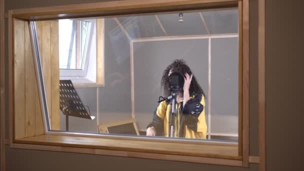 한 여성 예술가가 녹음실에서 유리 뒤에서 노래를 부른다. 힙합 가수가 노래를 녹음 하고 있습니다 — 비디오