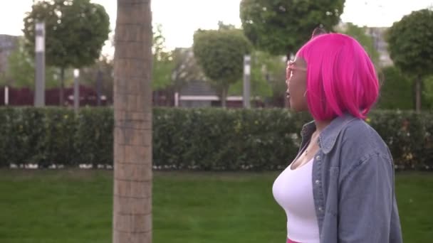 Молода приваблива чорна жінка з рожевим волоссям гуляє в парку — стокове відео