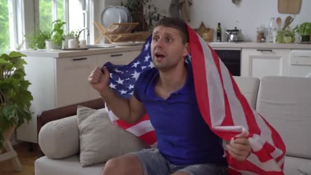 Amerykański fan ogląda telewizję w domu z flagą USA. mężczyzna amerykański sport fan wewnątrz — Wideo stockowe
