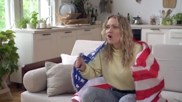 Mulher fã de esportes com bandeira dos EUA assistindo TV em casa. Futebol americano ou fã de esportes — Vídeo de Stock