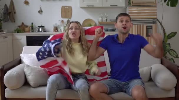 Famille couple de fans de football à la maison avec drapeau des États-Unis. Les fans de sport américains regardent la télévision à la maison sur le canapé — Video