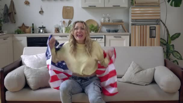 Amerikan bayrağı taşıyan kadın spor hayranı. Amerikalı bir kadın TV 'de spor programı izliyor. — Stok video