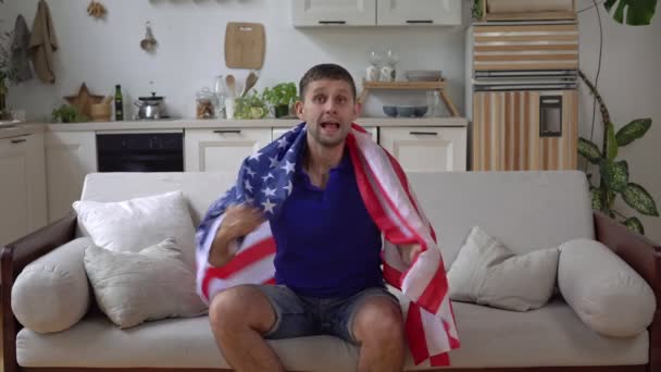 Ein männlicher Fan schaut zu Hause mit der USA-Flagge fern. Der amerikanische Sportfan jubelt über den Sieg — Stockvideo