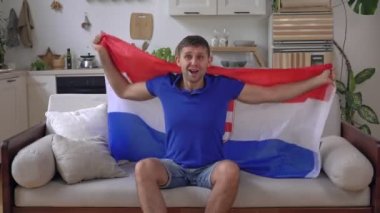 Hırvatistan bayrağıyla evde erkek spor taraftarı. Hırvat futbol taraftarı televizyon seyrediyor ve zafere seviniyor