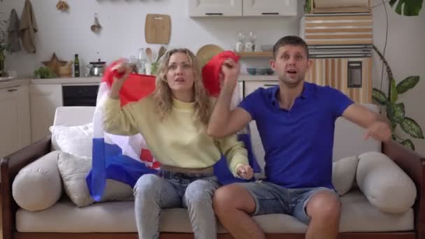 Família casal de fãs em casa com a bandeira da Croácia. Os fãs de futebol da seleção croata estão assistindo TV — Vídeo de Stock