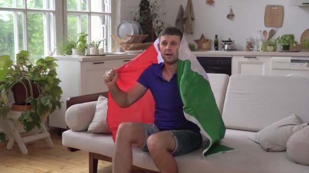 Άνδρας φίλαθλος στο σπίτι με τη σημαία της Ιταλίας. Ιταλός οπαδός του ποδοσφαίρου βλέπει τηλεόραση και χαίρεται για τη νίκη — Αρχείο Βίντεο
