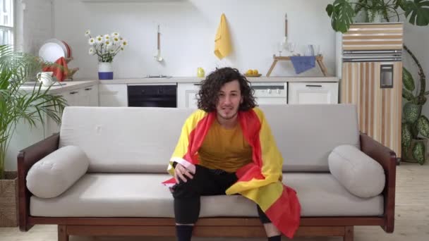 Een Spaanse voetbalfan kijkt thuis tv. Emotionele sportfan met de vlag van Spanje — Stockvideo