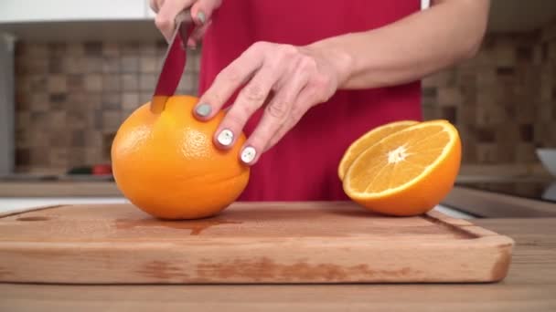 Uma mulher está cortando uma laranja suculenta madura na cozinha — Vídeo de Stock