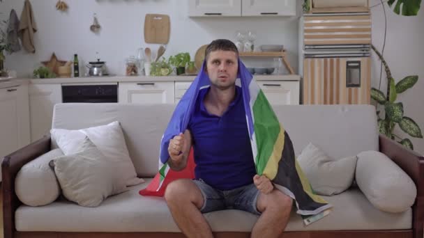 Biały fan sportu ogląda telewizję w domu z flagą RPA — Wideo stockowe