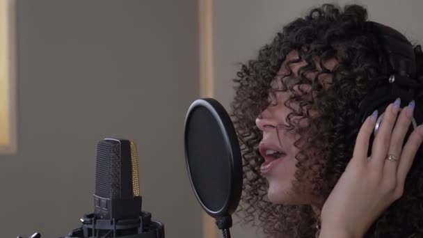 Крупный план молодой привлекательной певицы с микрофоном в студии звукозаписи — стоковое видео