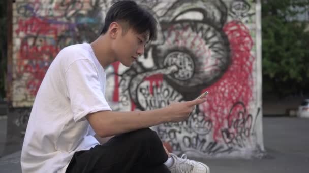 年轻的亚洲男人在城市街道上的智能手机。一个现代青少年的画像 — 图库视频影像