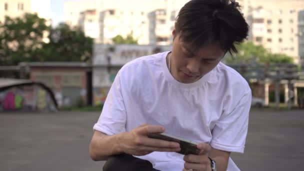 Genç Asyalı erkek oyuncu akıllı telefondan video oyunu oynuyor. Genç kız telefonda oynuyor. — Stok video