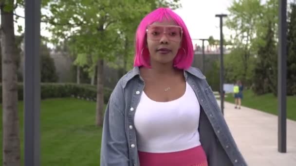 Wanita muda Afrika kulit hitam yang bahagia dengan rambut merah muda berjalan di taman — Stok Video
